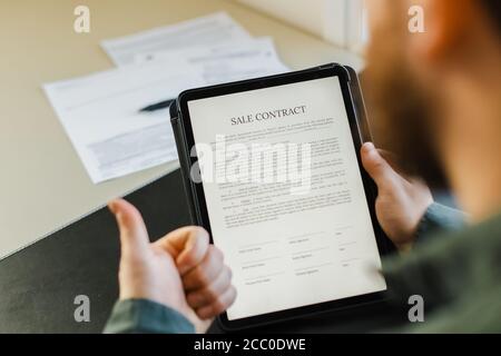 Mann unterzeichnet Kaufvertrag auf Tablet und zeigt Daumen nach oben. Stockfoto