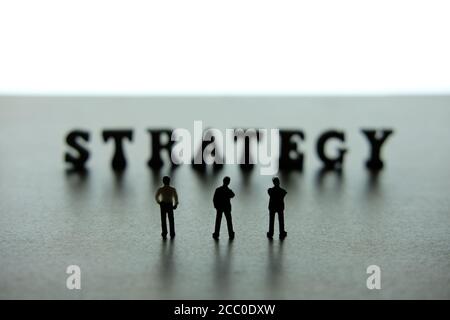 Silhouette von drei Miniatur-Geschäftsleute stehen auf Strategie Wort Block Puzzle Stockfoto