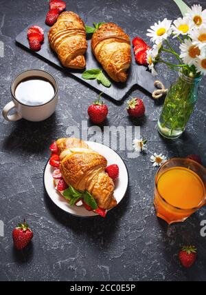 Leckeres Frühstück. Frische Croissants und Erdbeeren, schwarzer Kaffee und Orangensaft Stockfoto
