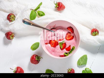 Erdbeereis in einer weißen Schüssel mit Erdbeeren auf weißem Holzhintergrund. Draufsicht Stockfoto