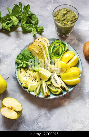 Frischer Salat mit Avocado, Kiwi, Apfel, Gurke, Birne, Limette und Minze mit Smoothie auf betontem Hintergrund. Gesundes Essen, Buddha Schüssel. Stockfoto