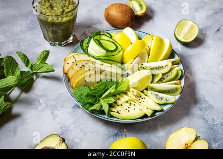 Frischer Salat mit Avocado, Kiwi, Apfel, Gurke, Birne, Limette und Minze mit Smoothie auf betontem Hintergrund. Gesundes Essen, Buddha Schüssel. Stockfoto