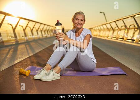 Fröhliche sportliche Frau sitzt auf Yoga-Matte im Freien Stockfoto