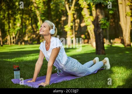 Fröhliche sportliche Frau praktiziert Yoga im Park Stockfoto