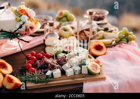 Nahaufnahme eines Schneidebretts mit Dorblue-Käse, Prosciutto, Kirschtomaten und Feigen auf einem Holztisch mit Früchten und einem weißen Hochzeitstorte auf einem Stockfoto