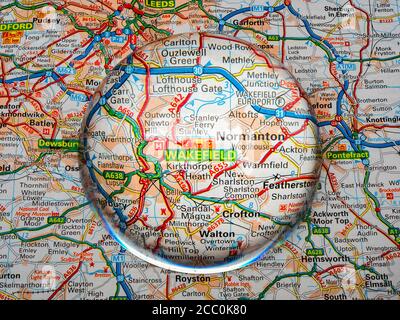 Nahaufnahme einer kuppelförmigen Lupe über einer Seite einer britischen Straßenatlas-Karte, mit der Wakefield-Gegend von England für eine genauere Ansicht vergrößert. Stockfoto