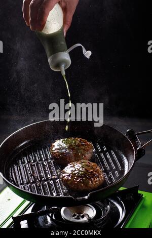 Der Koch röstet Burger für Burger. Gießt Öl auf eine heiße Pfanne. Stockfoto