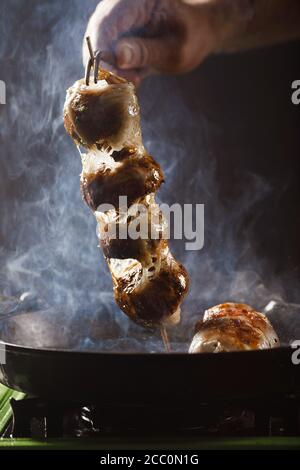 Der Koch röstet Champignons auf einem Spieß Stockfoto