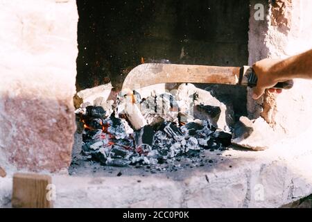 Der Koch legt brennende Kohlen mit einer Machete in den Grill. Stockfoto