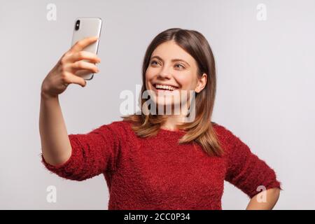 Portrait von fröhlichen hübschen Mädchen in zotteligen Pullover unter Selfie, so dass Videoanruf über Handy in der Hand, die Kommunikation mit Internet-fähigen Ele Stockfoto