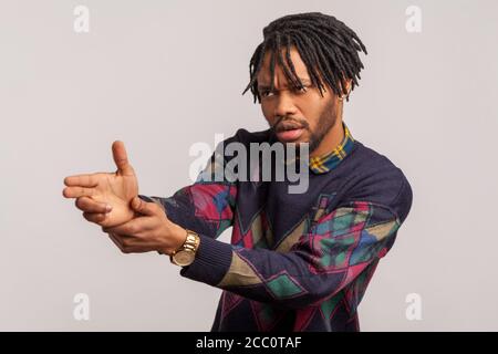 Ernst tapferer afrikanischer Mann mit Dreadlock im lässigen Stil Sweatshirt hält die Finger vorgeblich halten Waffe, Ziel Feind, Selbstverteidigung. Studio im Innenbereich Stockfoto