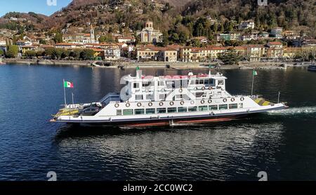 Luftdrohne Ansicht der Fähre, die aus dem Hafen von Laveno Mombello abfährt. Personentransport mit Fahrzeugen, Navigation auf dem Lago Maggiore, Italien Stockfoto