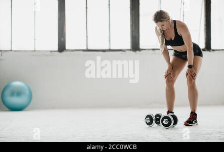 Müde Erwachsene Frau in Sportkleidung mit Fitness-Tracker Ruhe aus Übung mit Hanteln bei Tageslicht Stockfoto