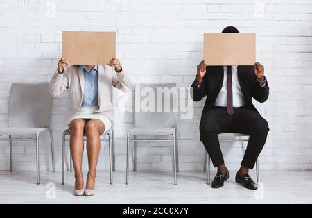 Afroamerikanische Jobbewerber schließen ihre Gesichter mit leeren Schildern im Büro des Unternehmens, Raum für Design Stockfoto