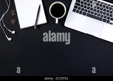 Computer, Kopfhörer, Stift und Tasse Kaffee auf schwarzem Tisch. Stockfoto