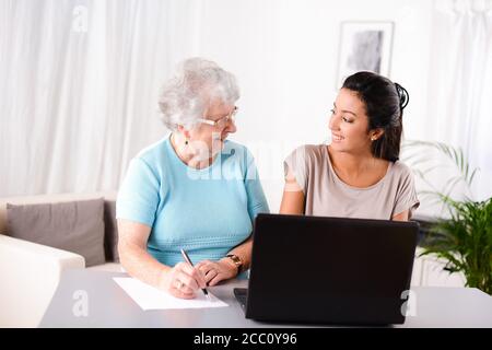 Fröhliche junge Frau hilft einem älteren älteren Menschen mit Laptop Computer für Internet-Suche und E-Mail Stockfoto