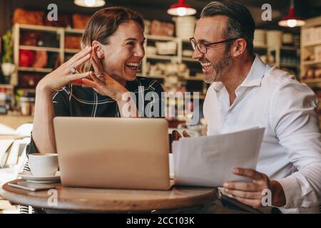 Lächelnder Geschäftsmann und Geschäftsfrau, die im Café mit Laptop und Dokumenten sitzen. Geschäftsleute, die im Café arbeiten. Stockfoto