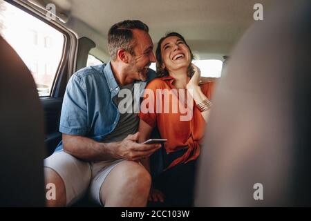 Glückliches Paar, das Spaß auf dem Rücksitz eines Autos hat. Mann und Frau, die mit dem Taxi unterwegs sind. Stockfoto