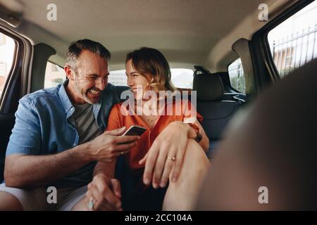 Schönes Paar auf dem Rücksitz des Autos. Liebevolles Paar mit einem Telefon, das in einem Taxi fährt. Stockfoto