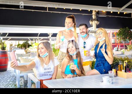 Freunde, die Selfie mit offenen Gesichtsmasken machen, während sie Alkohol trinken In der Cocktailbar Stockfoto