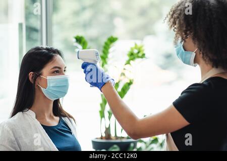 Frau Überprüfung der Temperatur zum Kunden mit Infrarot-Werkzeug in Schönheit Salon Stockfoto