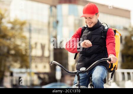 Happy Courier Überprüfung Der Zeit Auf Armbanduhr Sitzen Auf Fahrrad Im Freien Stockfoto