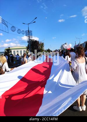 Minsk / Weißrussland - August 16 2020: Mädchen Demonstranten in Weiß mit einer riesigen weiß-rot-weißen Flagge auf der Straße in der Hauptstadt Stockfoto