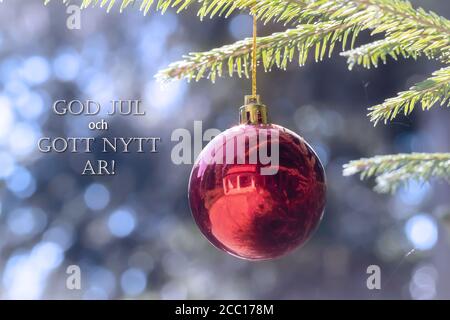 God Jul och Gott Nytt Ar bedeutet Frohe Weihnachten und glückliches Neues Jahr auf Schwedisch, Dänisch und Norwegisch. Rote Weihnachtskugel hängt am Weihnachtsbaum. Stockfoto