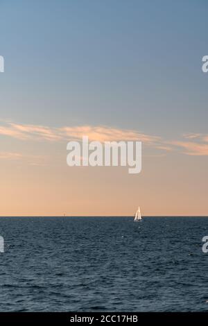 Weißes Segelboot auf einem ruhigen Meer oder Ozean während des Sonnenuntergangs. Großer Kopierspeicher. Minimalistischer Stil. Stockfoto