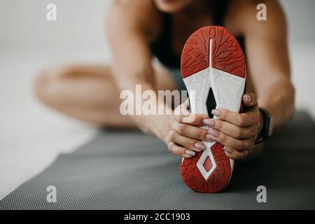 Frau in schwarzer Sportbekleidung mit Fitness-Tracker macht Gymnastik und Streckt ihre Beine auf der Matte Stockfoto