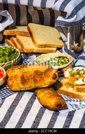 Rustikale Komposition mit Würstchenbrötchen, Spiegelei auf Toast, verschiedenen Schüsseln mit Sauce und gehacktem Gemüse. Stockfoto