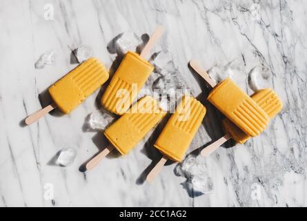 Flaches Lay von hausgemachten Mango Smoothie vegane Popsicles auf Marmor Hintergrund Stockfoto