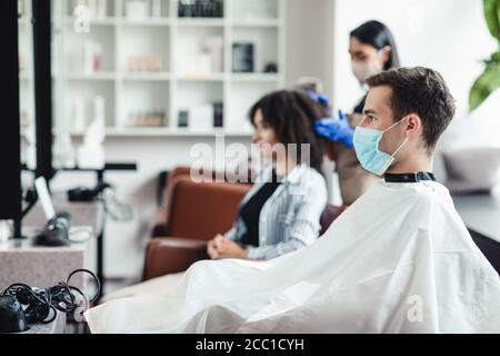 Mann in medizinischer Maske sitzt bei Friseuren, wartet auf Meister Stockfoto