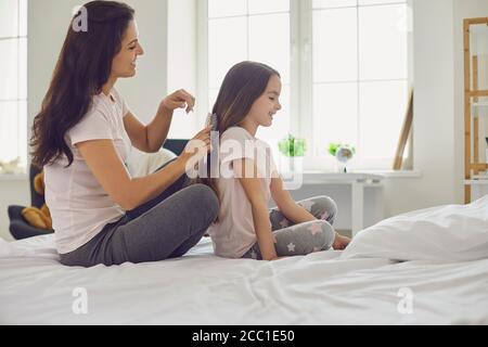 Mutter macht Frisur zu Mädchen Kind auf dem Bett im Schlafzimmer sitzen. Stockfoto