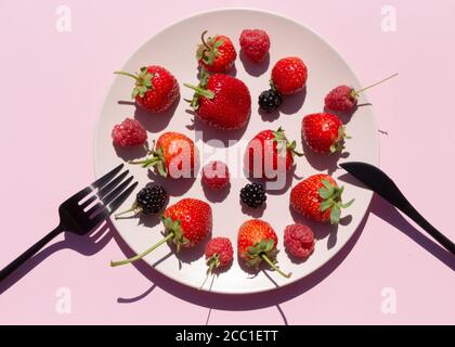 Frische Beeren, Erdbeeren, Himbeeren, Brombeeren in rosa Keramikplatte auf rosa Hintergrund. Vegetarische oder fruitarische Diät-Konzept. Stockfoto