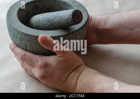 Die getrockneten Wurzeln der Heilkräuter werden von Hand in Steinmörtel gemahlen. Kaukasischer Mann mittleren Alters. Alternative Medizin. Heilkräuter. Stockfoto