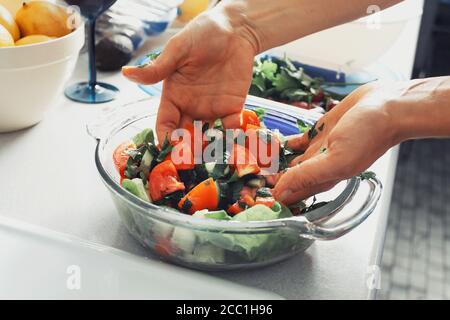 Hände einer Frau, die in einer Küche Salat macht, Gemüse mit Gewürzen in einer Schüssel vermischt Stockfoto