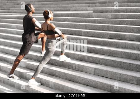 Motiviertes Schwarzes Paar, Das Muskeln Aufwärmt, Bevor Es Im Freien Joggt Städtische Treppe Stockfoto