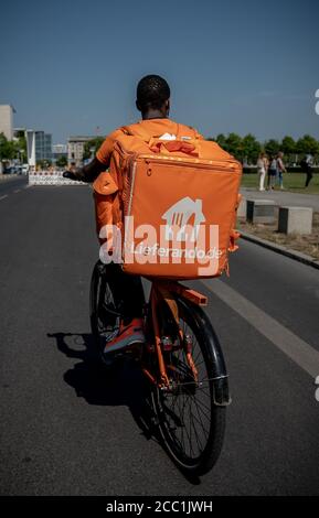 Berlin, Deutschland. August 2020. Ein Kurier des Lebensmittellieferdienstes Lieferando fährt mit seinem Rucksack am Sitz des Deutschen Bundestages, dem Reichstagsgebäude, vorbei. Quelle: Michael Kappeler/dpa/Alamy Live News Stockfoto