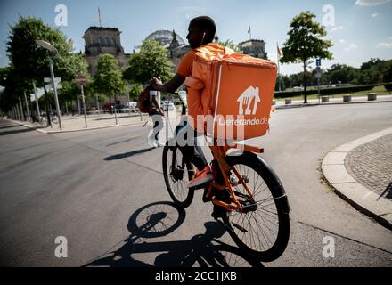 Berlin, Deutschland. August 2020. Ein Kurier des Lebensmittellieferdienstes Lieferando fährt mit seinem Rucksack am Sitz des Deutschen Bundestages, dem Reichstagsgebäude, vorbei. Quelle: Michael Kappeler/dpa/Alamy Live News Stockfoto