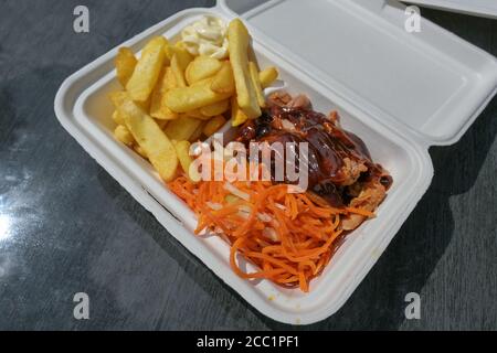 Schweinefleisch in einer Take-Away-Box mit Grillsoße, Krautsalat und Karottensalat, pommes Frites und Mayo-Schnellimbiss auf einem Tisch in einem Straßenrestaurant Stockfoto