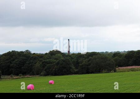 Ein Blick auf Barrow Bridge Chimney mit einem Wald und Feld mit rosa Heuballen vor dem Winter Hill, England Stockfoto