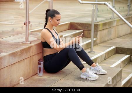 Fit junge Frau trägt Sportkleidung sitzen unten draußen und überprüfen ihr Telefon. Stockfoto