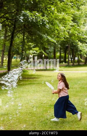 Vertikale voller Länge Porträt von sorglosen Mädchen läuft im Park im Freien beim Spielen mit Blasen und halten große Blase Zauberstab, kopieren Raum Stockfoto