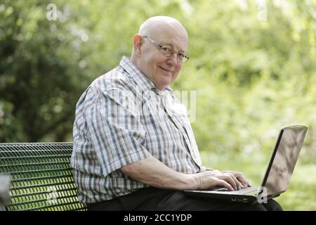 Deutschland, Nordrhein-Westfalen, Köln, Porträt von älteren Mann mit Laptop auf der Bank im Park, Lächeln Stockfoto