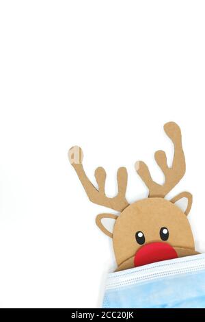 Pappausschnitt von Rudolph, dem rotnasigen Rentier, der beim Tragen einer Gesichtsmaske guckt. Covid während der Weihnachtszeit Konzept. Weißer Hintergrund, portrai Stockfoto