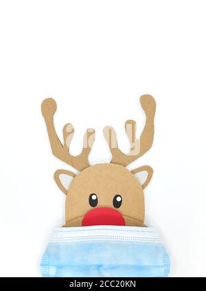 Pappausschnitt von Rudolph, dem rotnasigen Rentier, der beim Tragen einer Gesichtsmaske guckt. Covid während der Weihnachtszeit Konzept. Weißer Hintergrund, portrai Stockfoto