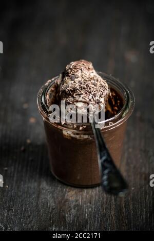 Glas und Löffel von Schokoladenpudding mit Vanillesauce auf Holztisch, Nahaufnahme Stockfoto