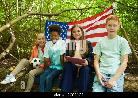 Multiethnische Gruppe von Kindern, die unter Ästen eines großen Baumes sitzen und im Wald oder Garten spielen, kopieren Sie den Raum Stockfoto