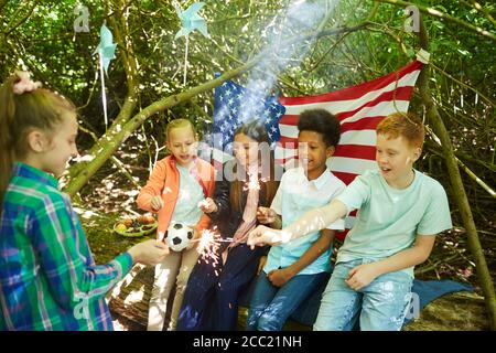 Multiethnische Gruppe von Kindern Beleuchtung Wunderkerzen, während sich unter Ästen von großen Bäumen im Wald oder spielen im Hinterhof, kopieren Raum Stockfoto